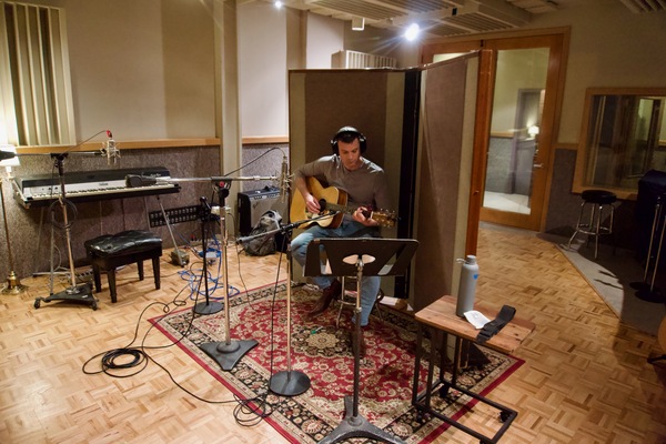 A man recording acoustic guitar in a studio